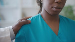 man in lab coat with hand on woman in scrubs shoulder - dental practice sexual harassment concept