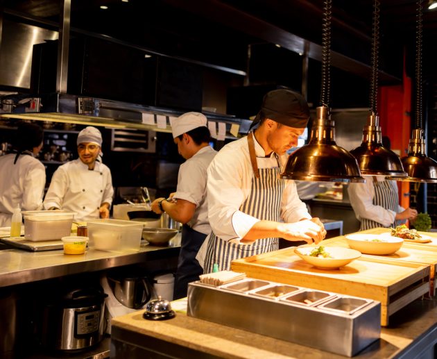 Latin American chef decorating a plate under a hot lamp while working at a commercial kitchen