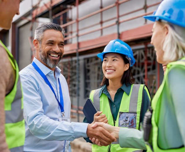 Smiling construction professionals exchanging a handshake as part of their partnership on site. Happy engineer shaking hands at construction site with happy businessman. Handshake between middle eastern construction manager with architect at building site, conclude an agreement.