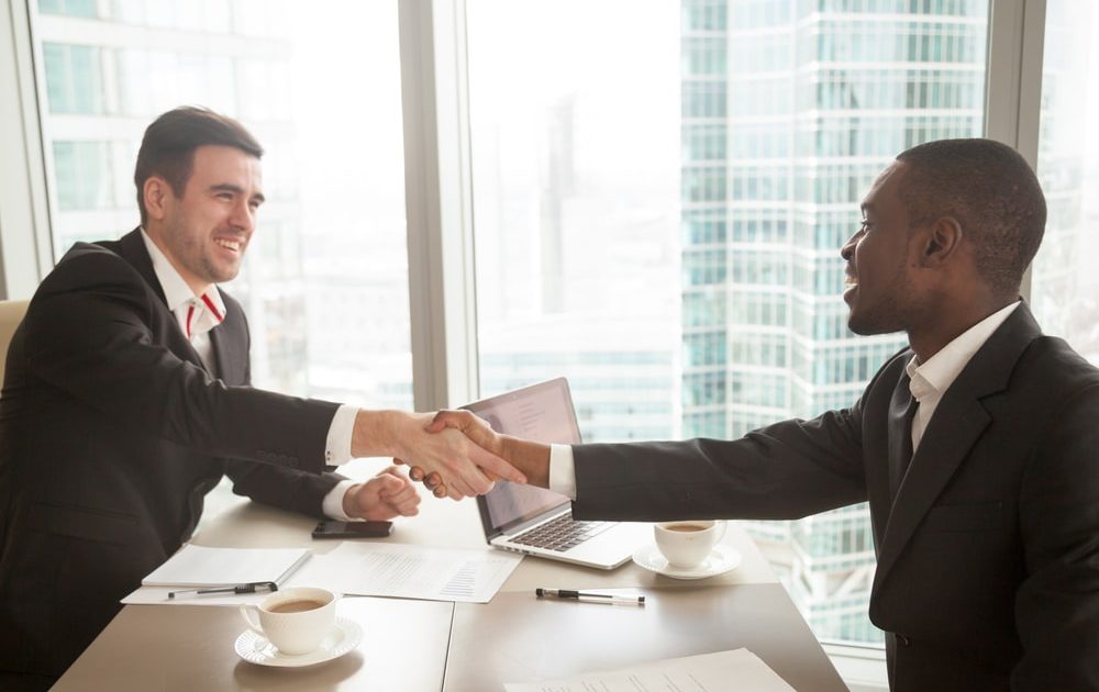 Two,Satisfied,Multiracial,Businessmen,Shaking,Hands,Over,Office,Desk,,Handshaking