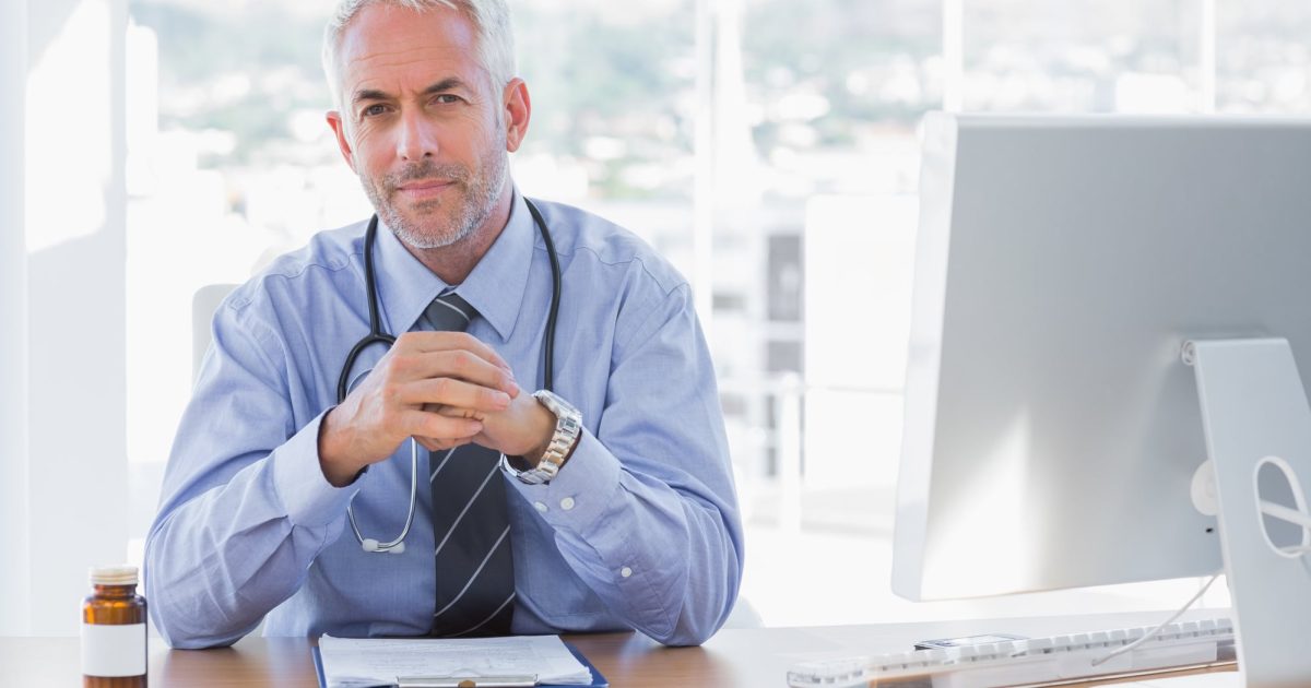 Serious doctor sitting at his desk and looking at camera