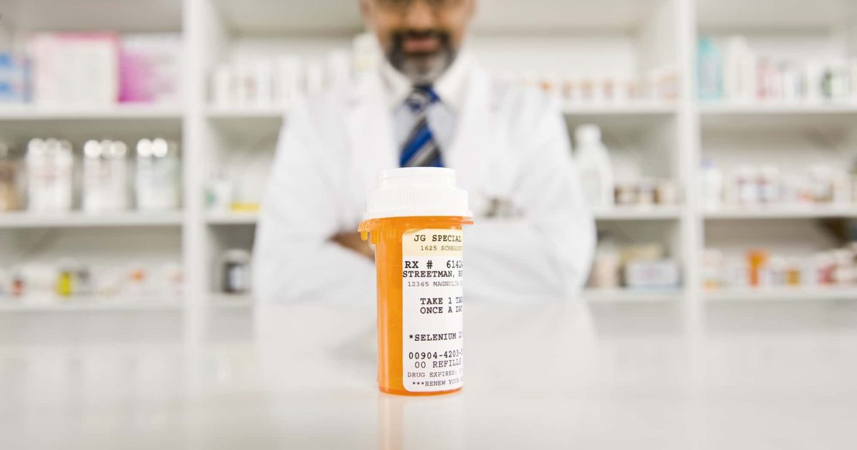 Bottle Of Pills On Desk With Pharmacist In Drugstore