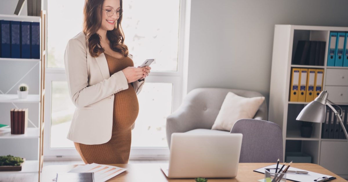 Photo portrait of pregnant woman holding phone in two hands typing standing in modern office