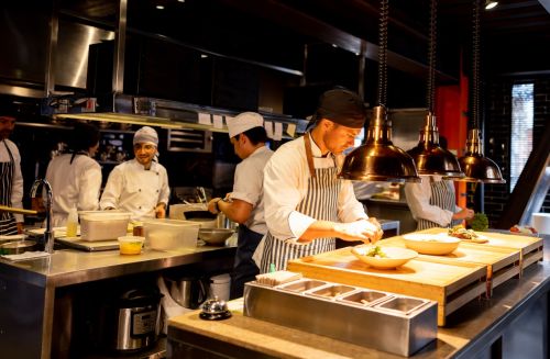 Latin American chef decorating a plate under a hot lamp while working at a commercial kitchen