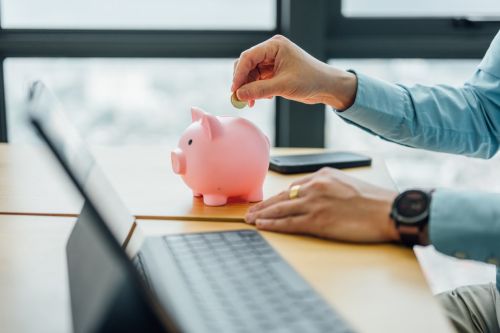 An Asian Chinese businesswoman puts a gold coin into a piggy bank in the office — a concept of saving and investment.